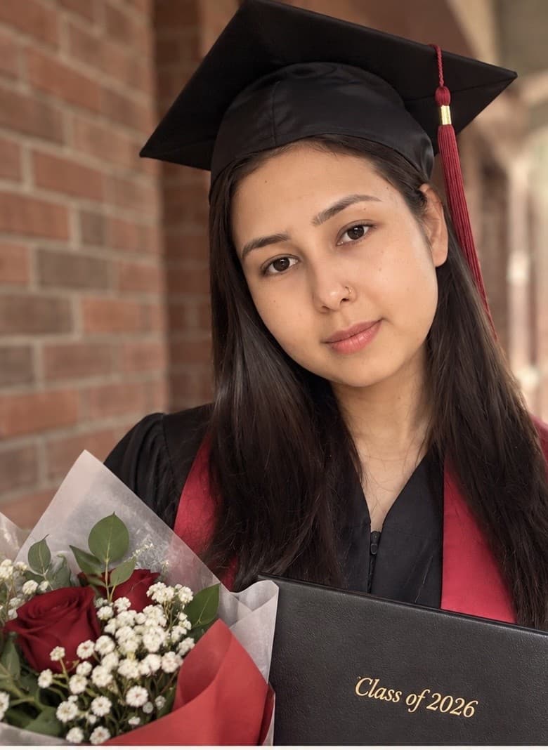 Mursal Dost in cap and gown on graduation day, holding a diploma and a bouquet of roses